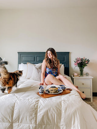 a person sitting on a bed with a cat and a tray of food