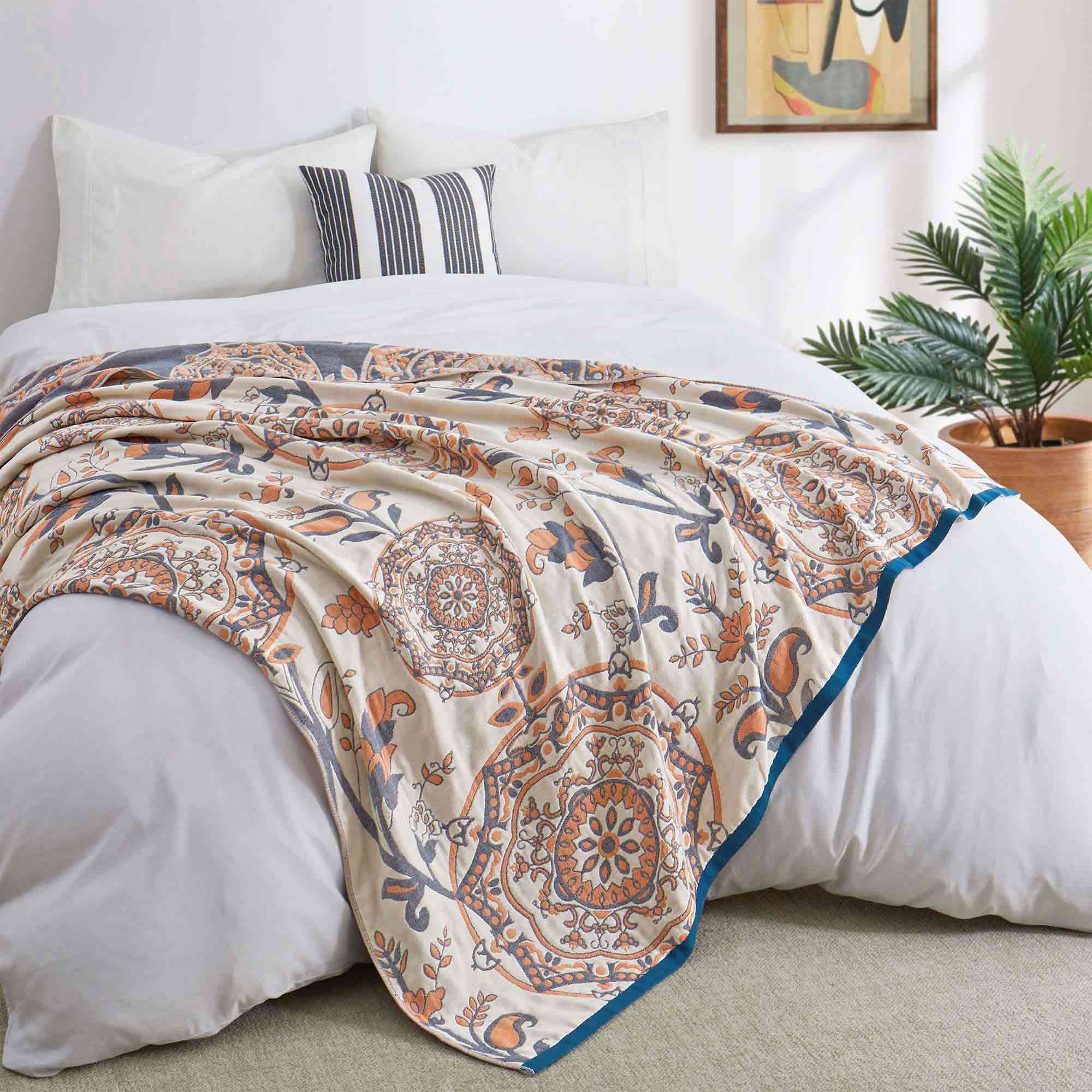 Cream-colored velvet throw blanket with intricate orange and navy medallion and vine patterns, finished with a navy blue border.