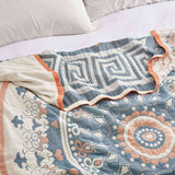 Cream-colored velvet throw blanket with intricate orange and navy medallion and vine patterns, finished with a navy blue border.