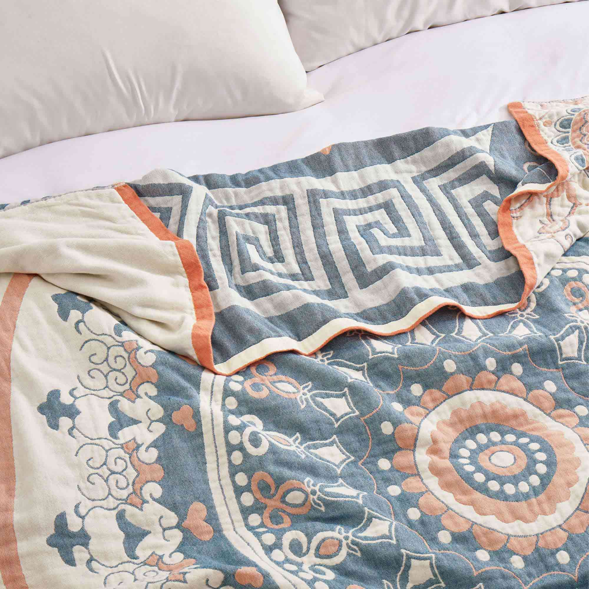 Cream-colored velvet throw blanket with intricate orange and navy medallion and vine patterns, finished with a navy blue border.