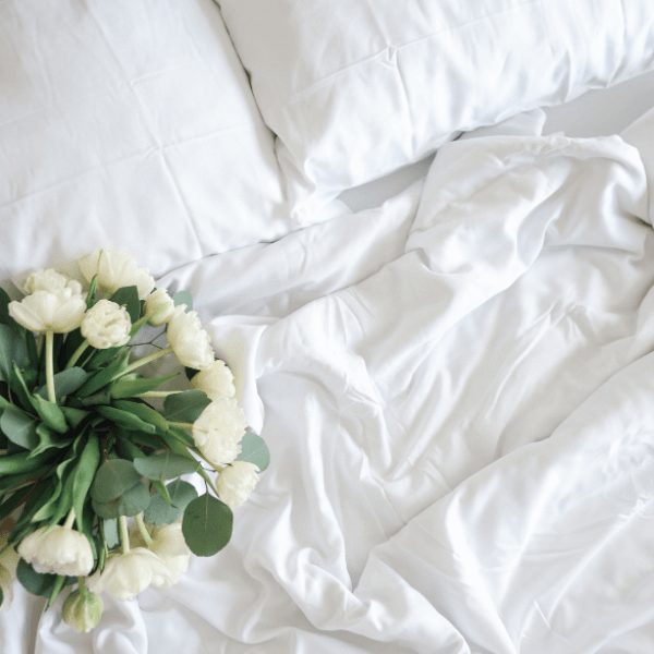 White tulips on an unmade bed with white sheets and pillows.