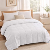 A neatly made bed with hotel-inspired bedding, featuring crisp white linens, pillows, a plush Cotton Oversized Down Blanket in white, a beige throw pillow, and light wood furniture in a sunlit room.