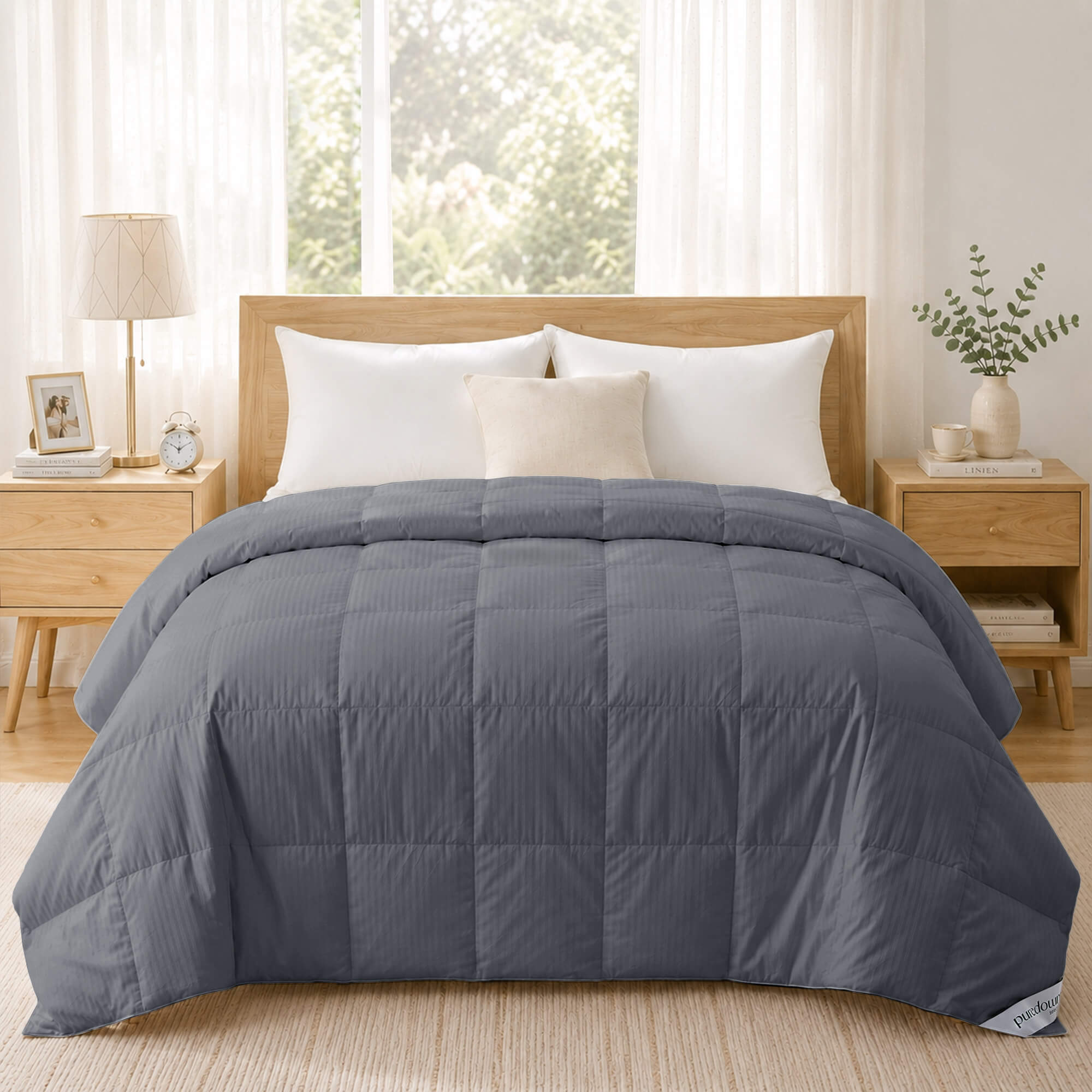 A neatly made bed with a gray comforter, white pillows, and light wood furniture features the Cotton Oversized Down Blanket, crafted from 380 thread count cotton, in a bright bedroom.