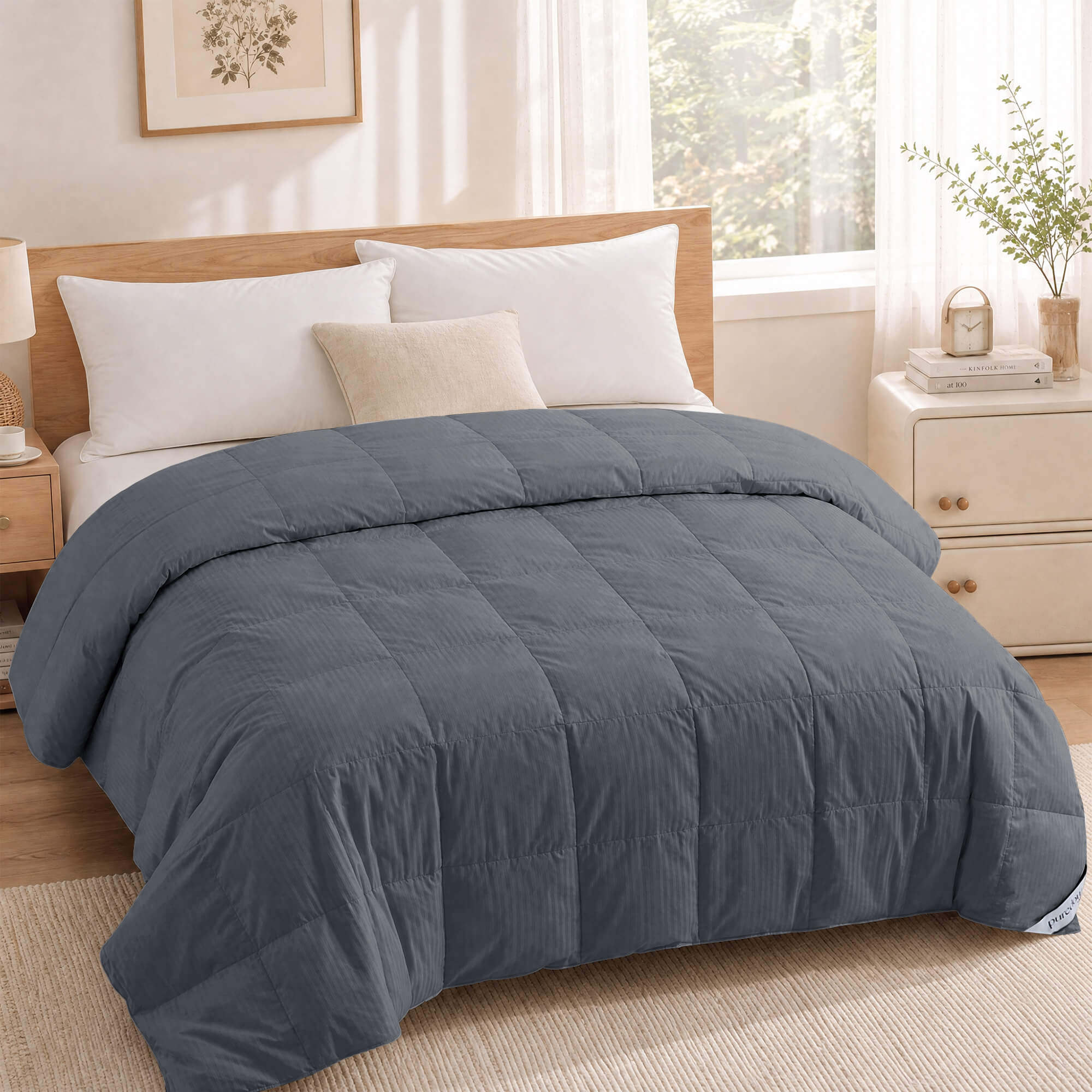 A neatly made bed with a gray comforter, the Cotton Oversized Down Blanket in premium white, and white pillows rests against a wooden headboard in a bright bedroom, while soft 380 thread count cotton adds a touch of luxury.