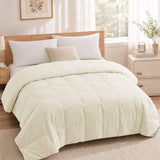 A sunlit, minimal bedroom with wooden furniture features a beige bed topped with white pillows and the Cotton Oversized Down Blanket in premium white.