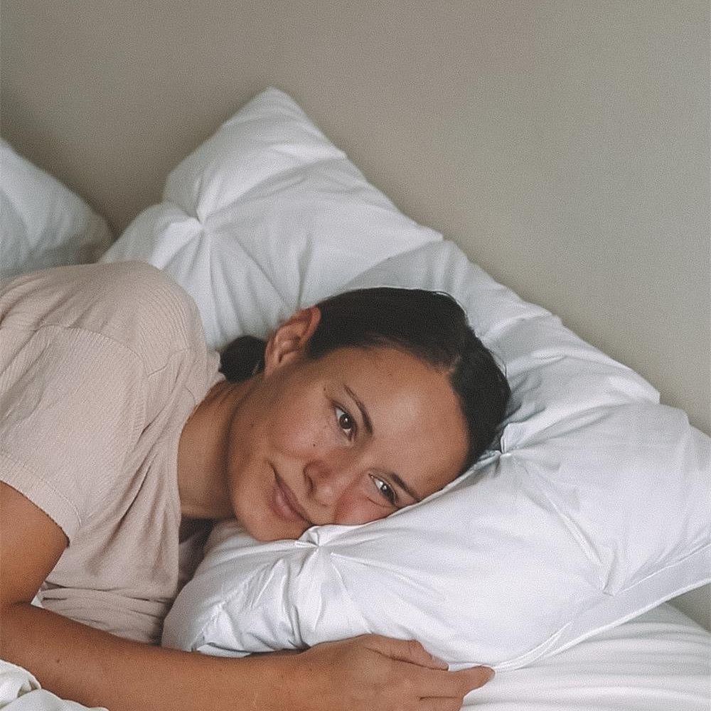 A woman lying in bed, resting her head on a white pillow and looking thoughtfully into the distance.