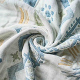 Twisted into a gentle spiral, the Boho Cotton Throw Blanket showcases a white fabric adorned with blue, green, and yellow geometric patterns—a vibrant multi-color design aesthetic perfect for lovers of boho throw blankets.