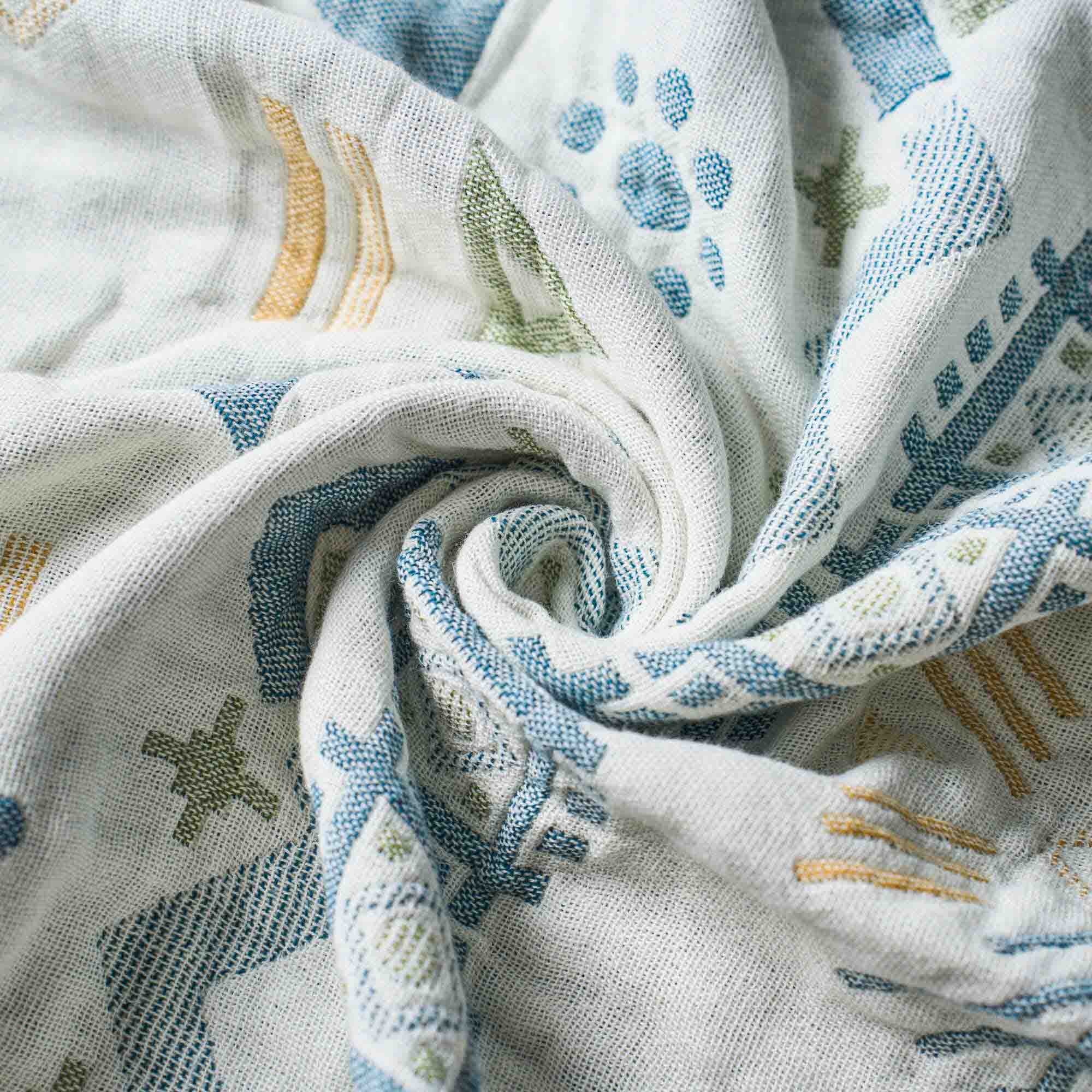 Twisted into a gentle spiral, the Boho Cotton Throw Blanket showcases a white fabric adorned with blue, green, and yellow geometric patterns—a vibrant multi-color design aesthetic perfect for lovers of boho throw blankets.
