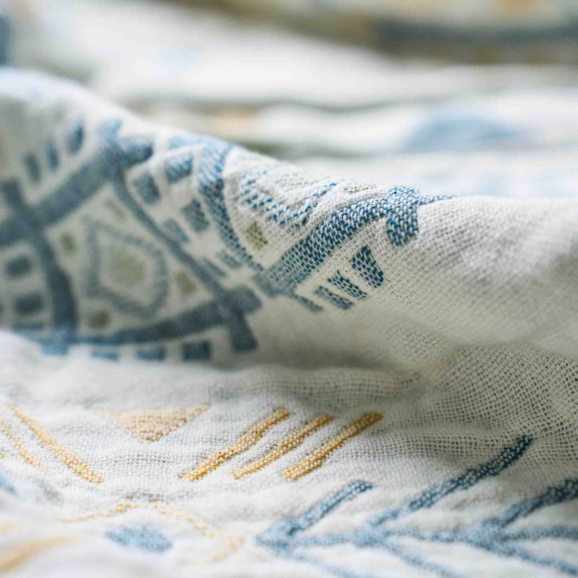 Close-up of white fabric with blue and gold geometric embroidery, highlighting the texture and detail—ideal for the Boho Cotton Throw Blanket, which features an intricate, multi-color design in a cotton jacquard weave.