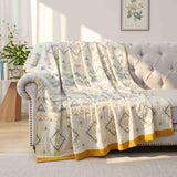 The Boho Cotton Throw Blanket, featuring a multi-color jacquard design and yellow trim, is draped over a beige tufted sofa in a bright living room.