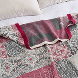 The Boho Cotton Throw Blanket, featuring a red, gray, and white floral jacquard pattern, is spread across a white bed with pillows.