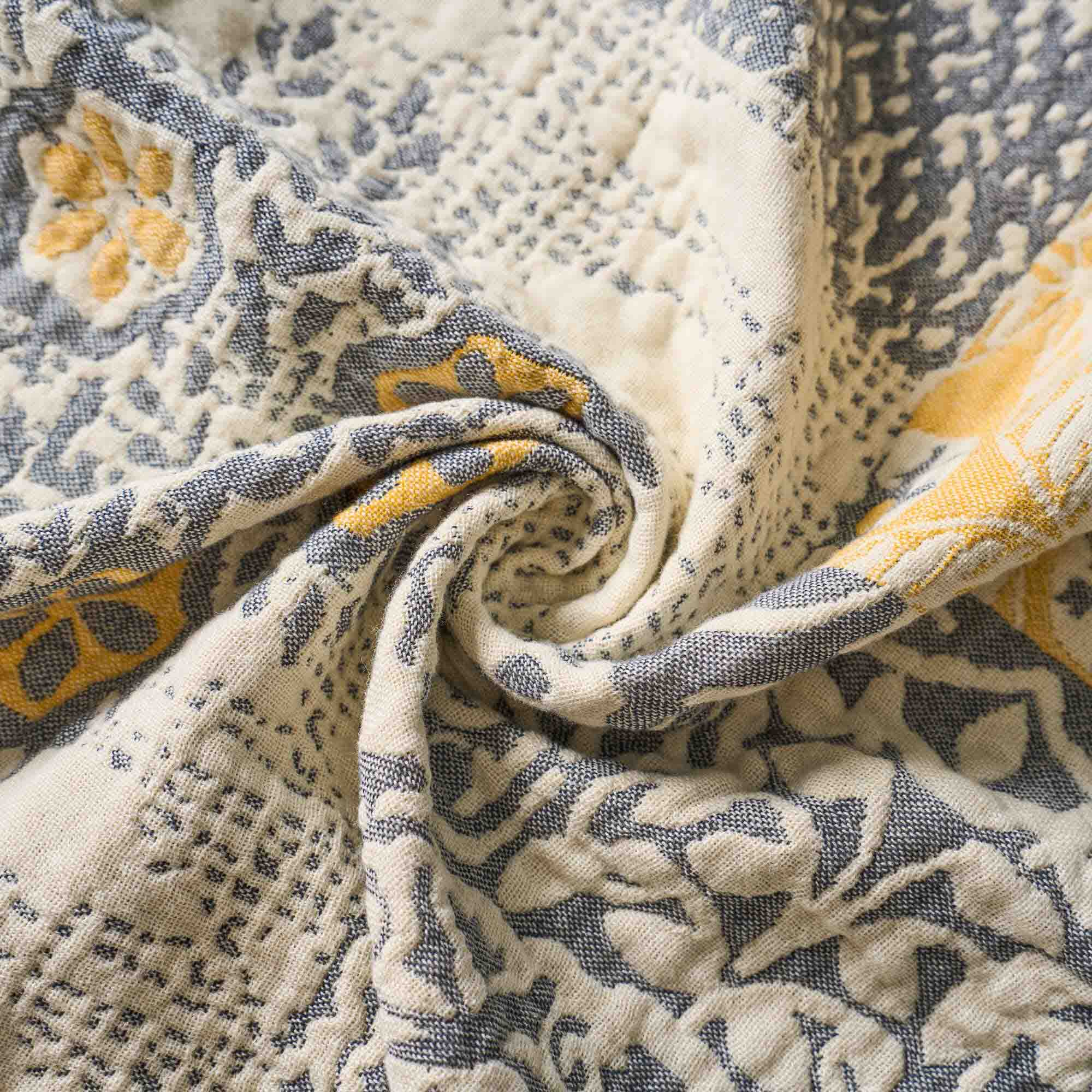 Close-up of the Boho Cotton Throw Blanket, crafted from textured jacquard cotton fabric with gray, yellow, and cream floral patterns, softly twisted at the center for a cozy and stylish boho accent.