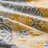 The Boho Cotton Throw Blanket, featuring a yellow and gray jacquard pattern with floral and geometric designs, is displayed in soft, gentle folds to add a touch of elegance to any space.