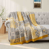 A Boho Cotton Throw Blanket featuring a gray and yellow pattern is draped over a light gray tufted sofa in a cozy living room.