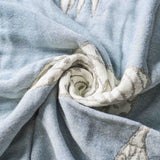 Light blue and white fabric with a swirl fold, showing texture and subtle pattern details—the Boho Cotton Throw Blanket offers both style and comfort to your living space.