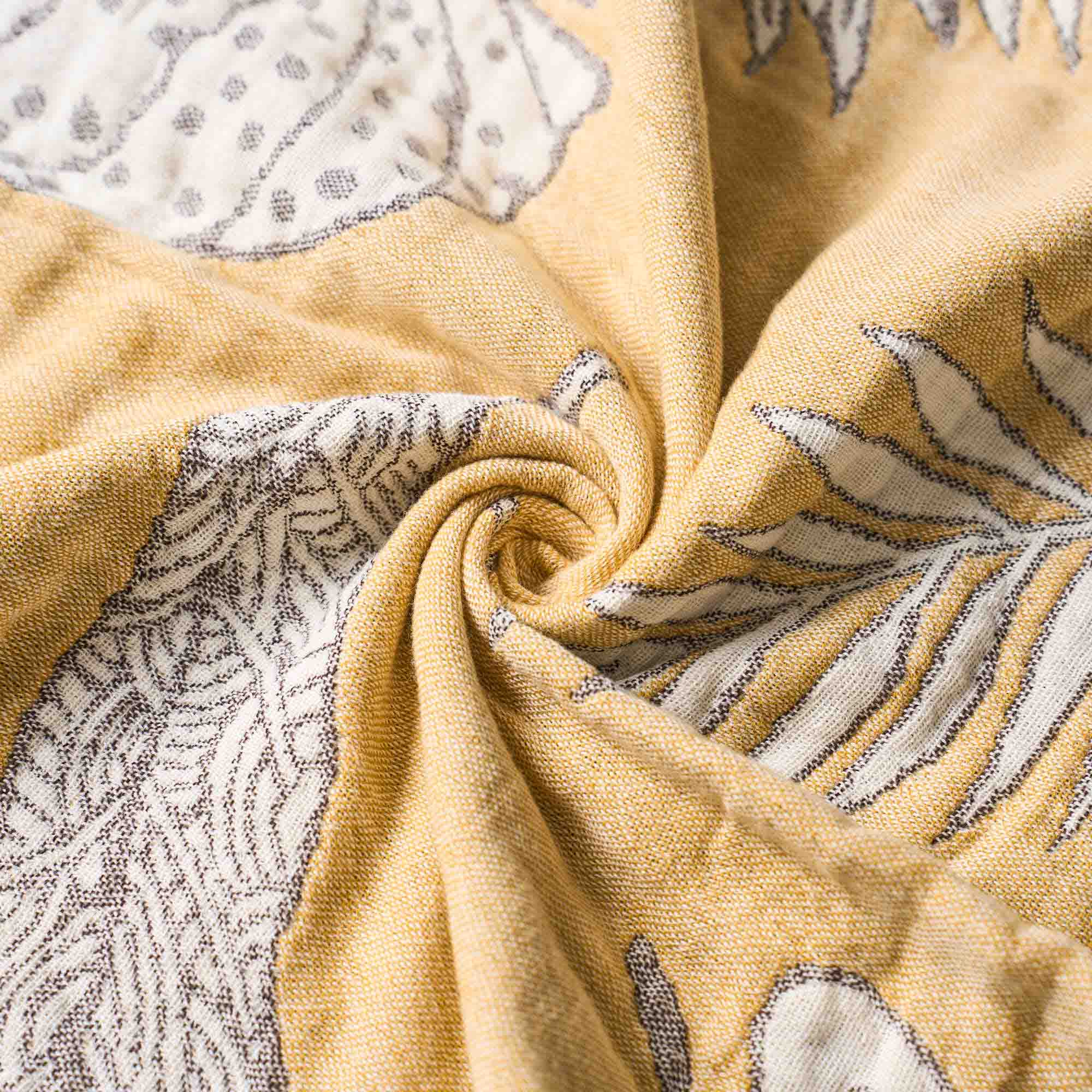 Beige and white patterned fabric twisted into a spiral, showing detailed texture and fine line designs—this Boho Cotton Throw Blanket adds a touch of elegance to any space.