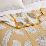 A Boho Cotton Throw Blanket with yellow and white leaf jacquard patterns is spread on a bed with white pillows.