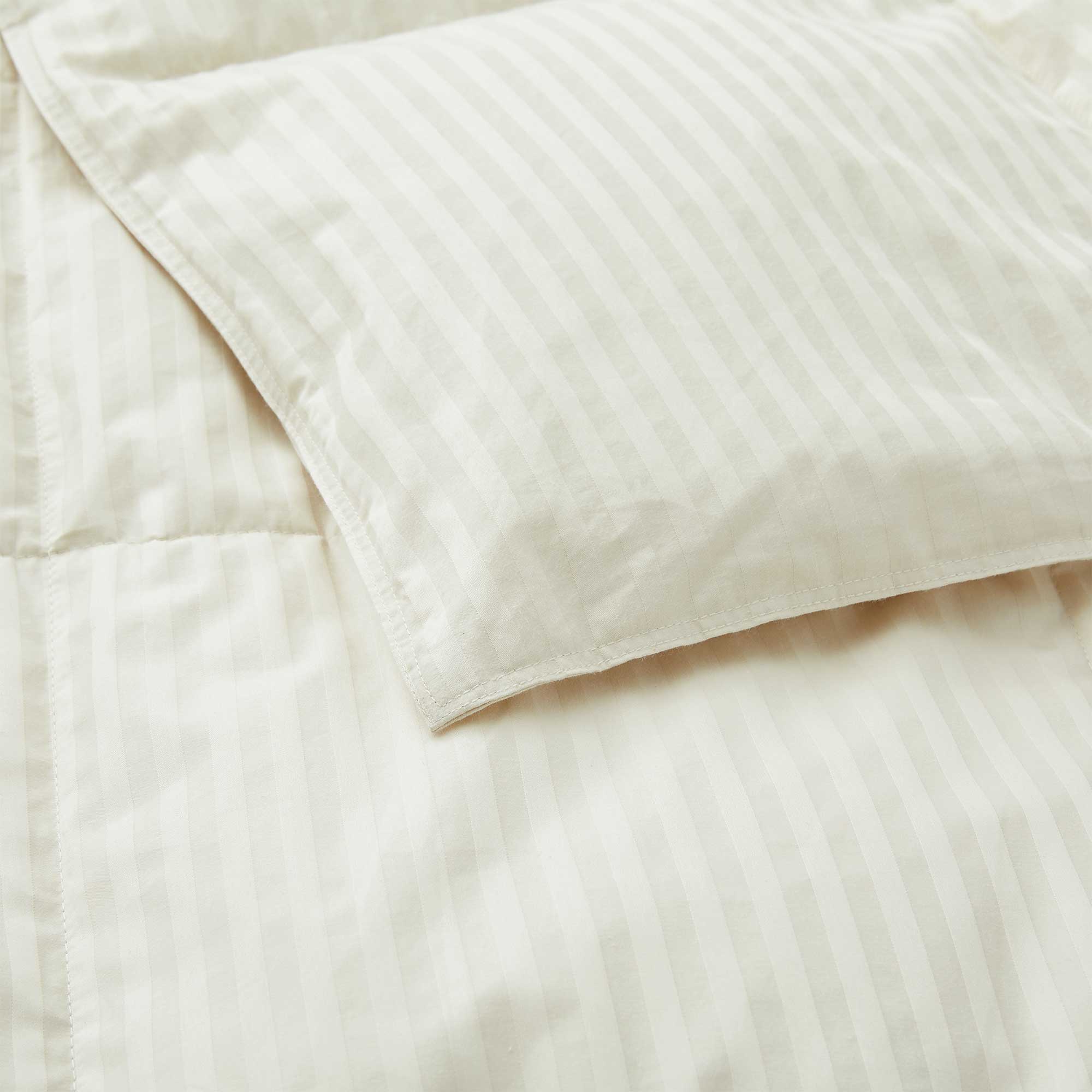 Woven Stripe Down Blanket in a cream color with stripes, elegantly displayed on a neatly made bed.
