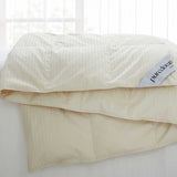 A Woven Stripe Down Blanket in a cream color is draped over a white couch in a softly lit room.
