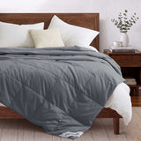 A neatly made bed features the Woven Stripe Down Blanket, paired with white pillows and a wooden headboard beside a small nightstand.