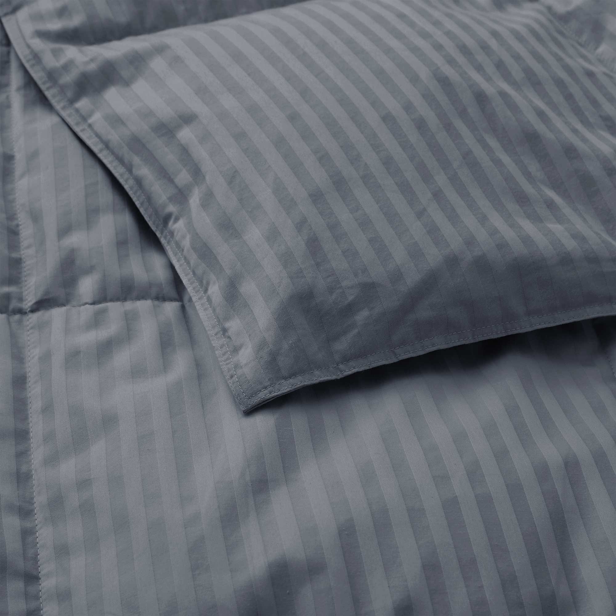 Close-up of a Woven Stripe Down Blanket in gray atop a neatly made bed, paired with a matching striped pillow.