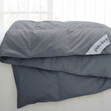 A Woven Stripe Down Blanket in dark gray with a puredown label is draped over a white couch near a window.