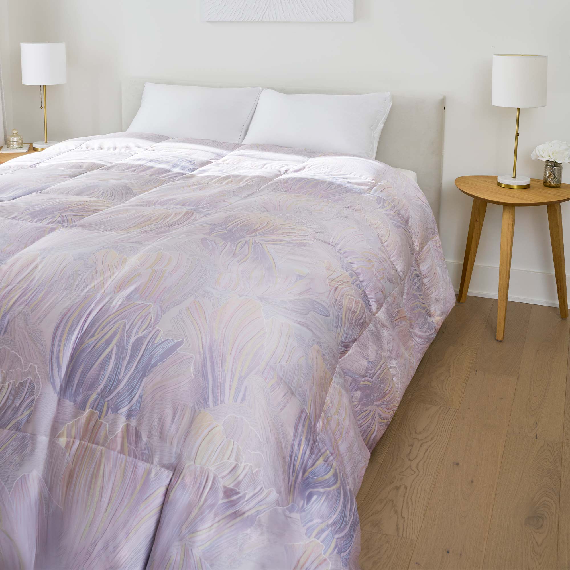 A neatly made bed with a pastel-patterned comforter, flanked by round wooden nightstands and white lamps.