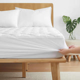 A hand stretches the Organic Cotton Waterproof Mattress Pad over a bed with a wooden frame and white bedding.