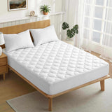 A neatly made bed with white bedding and an Organic Cotton Waterproof Mattress Pad in a bright, modern bedroom filled with plants and large windows.