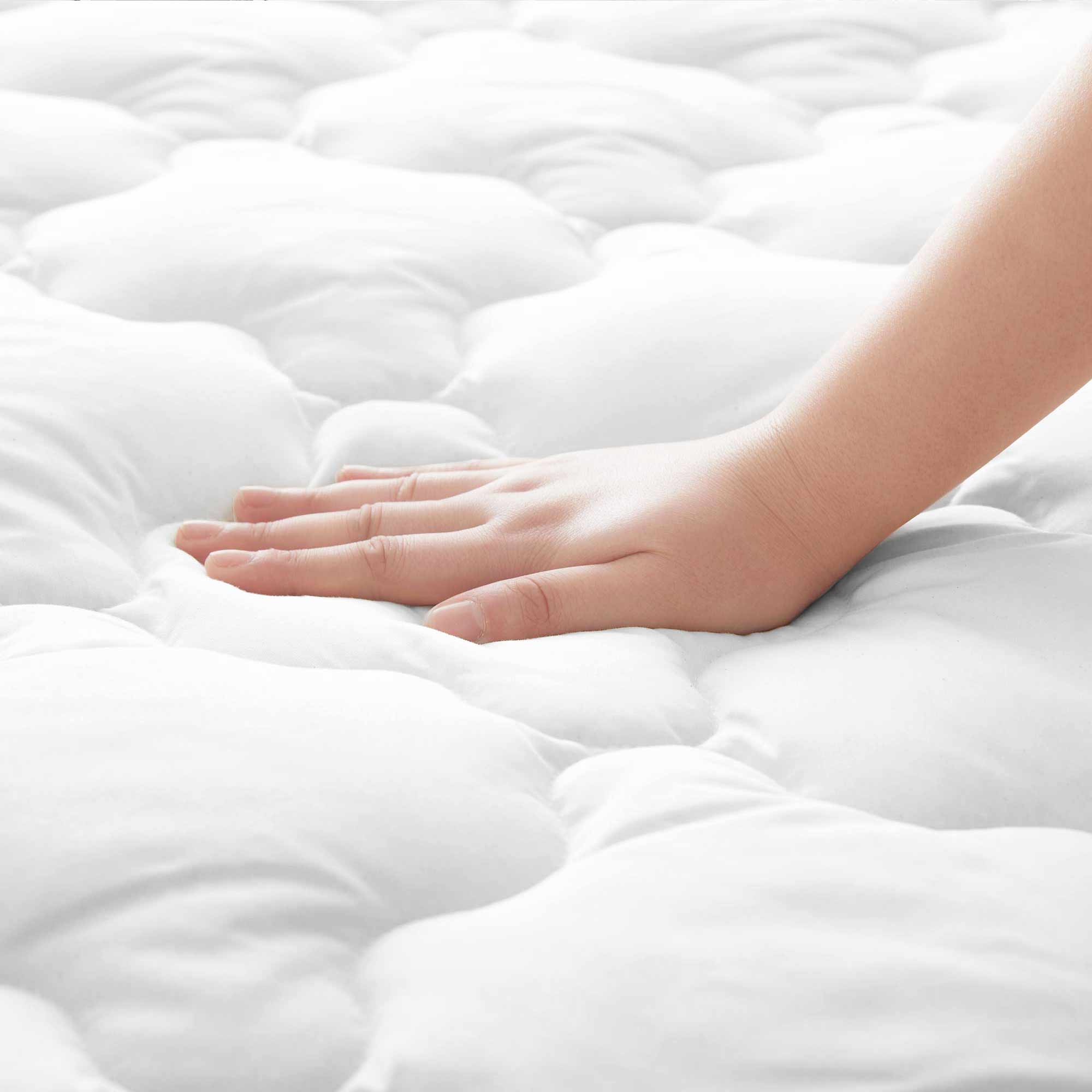 A hand presses down on a soft, white, quilted Organic Cotton Waterproof Mattress Pad.