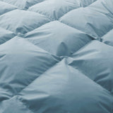Close-up of a light blue, quilted surface of the Premium Goose Feather Comforter, showcasing its puffy and plush fabric texture.