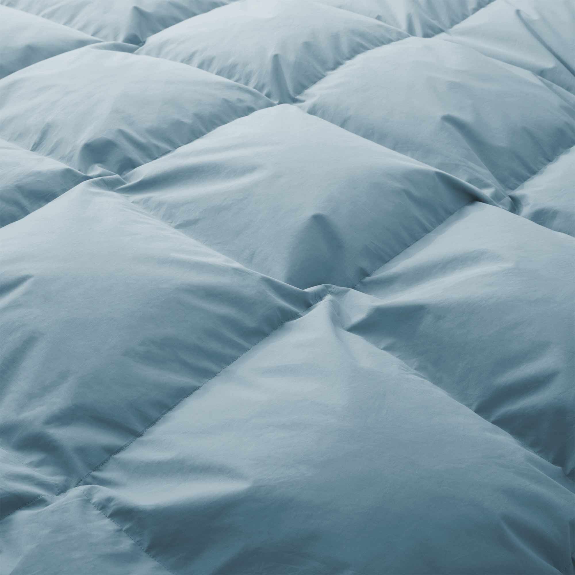 Close-up of a light blue, quilted surface of the Premium Goose Feather Comforter, showcasing its puffy and plush fabric texture.
