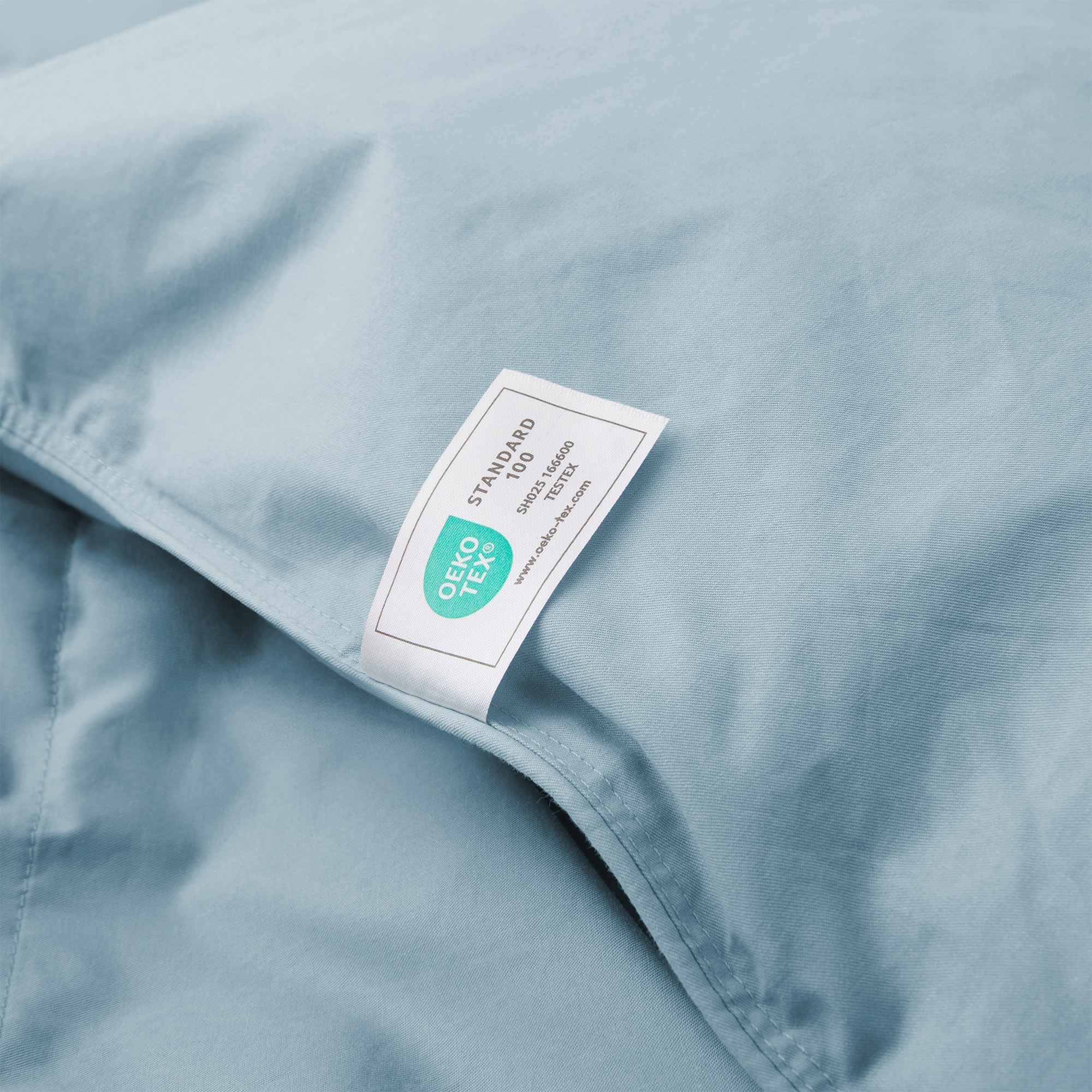 A close-up of the Premium Goose Feather Comforter in blue fabric, featuring an attached Oeko-Tex Standard 100 label.