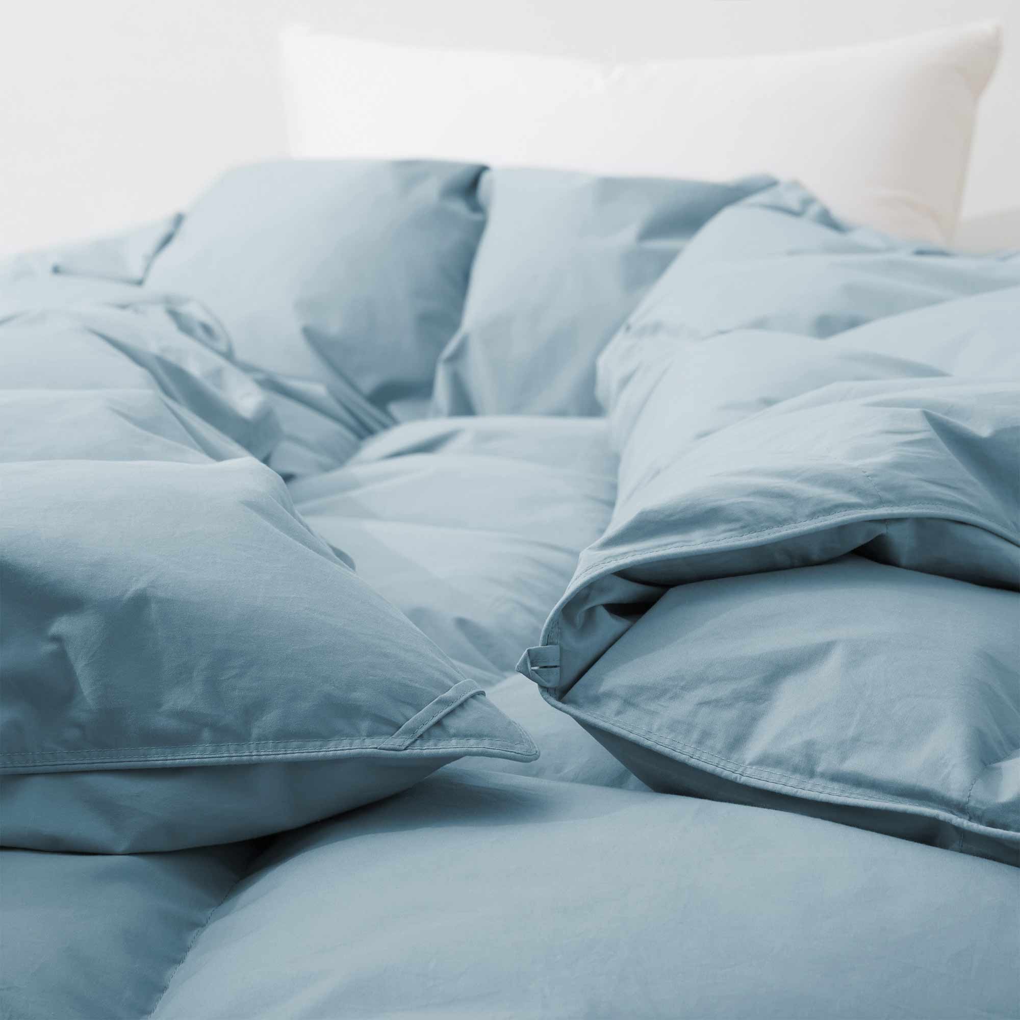 Premium Goose Feather Comforter in light blue on a bed with a white pillow in the background.