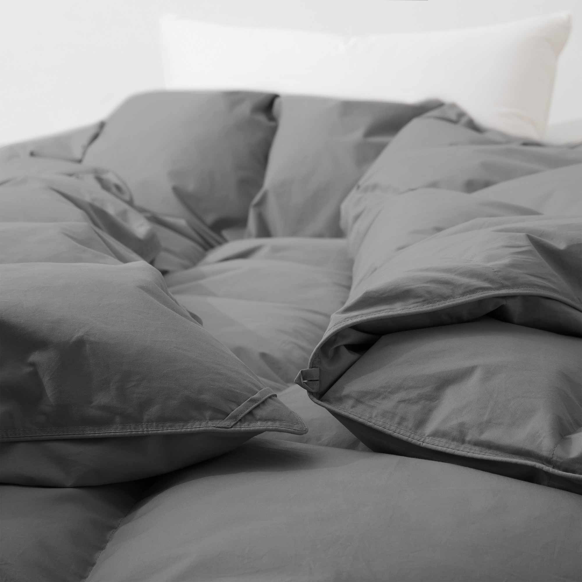 Close-up of the Premium Goose Feather Comforter in gray on a bed, with a white pillow in the background.