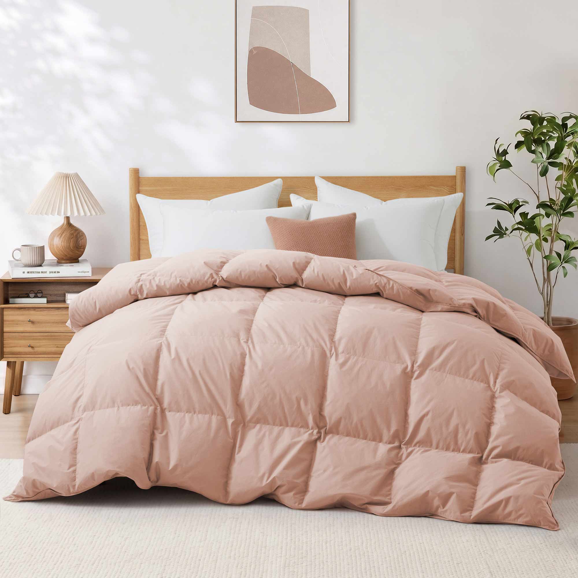 A neatly made bed featuring the Premium Goose Feather Comforter in pink, complemented by pillows, a wooden headboard, and a nightstand with a lamp.