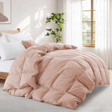 A neatly made bed features the Premium Goose Feather Comforter in light pink, set in a bright, airy bedroom with large windows and a plant.