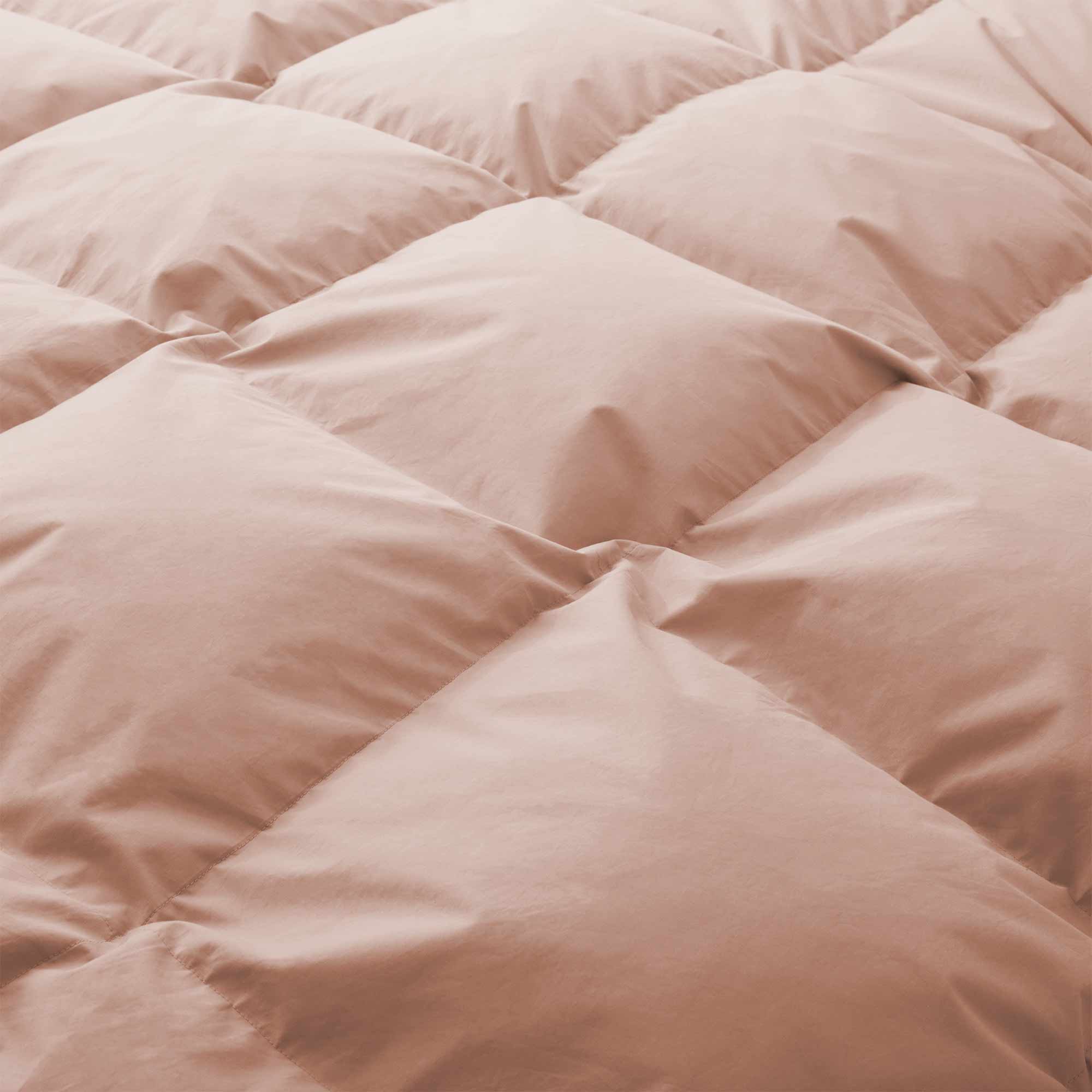 Close-up of the Premium Goose Feather Comforter, featuring a soft, peach color and a puffy, quilted square pattern.