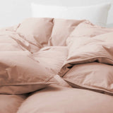A Premium Goose Feather Comforter in a soft, light brown color with fluffy, quilted sections is displayed on a white bed with a white pillow behind it.