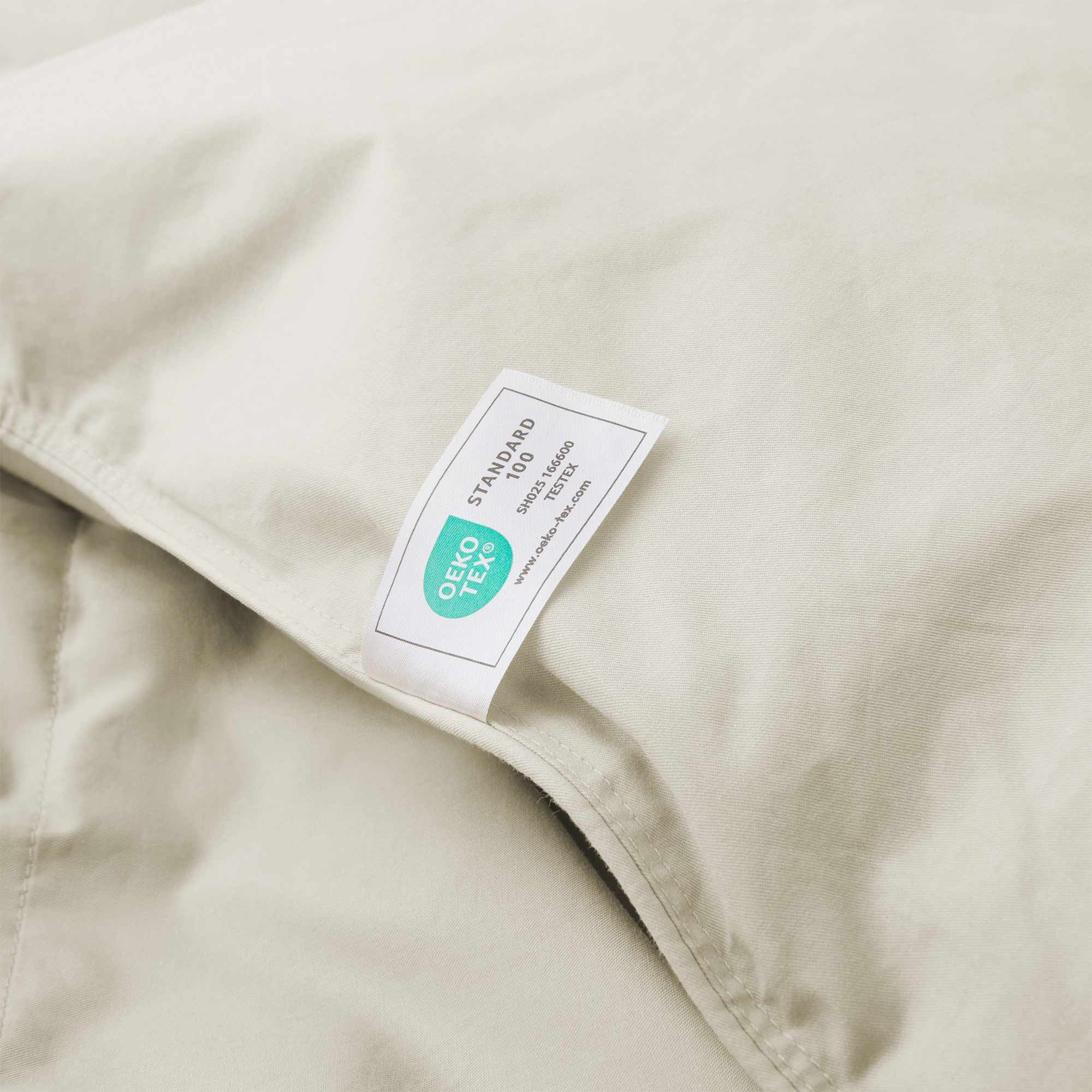 A close-up of the Premium Goose Feather Comforter in beige fabric, featuring a white and green OEKO-TEX Standard 100 certification label.