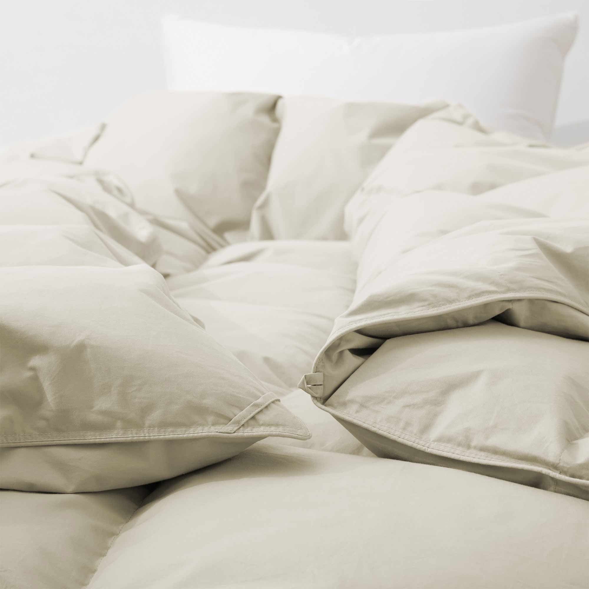 Close-up of the Premium Goose Feather Comforter in beige, featuring a fluffy texture on a bed with a white pillow in the background.