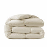 A Premium Goose Feather Comforter, elegantly folded in a cream hue, is stacked neatly on a white surface.