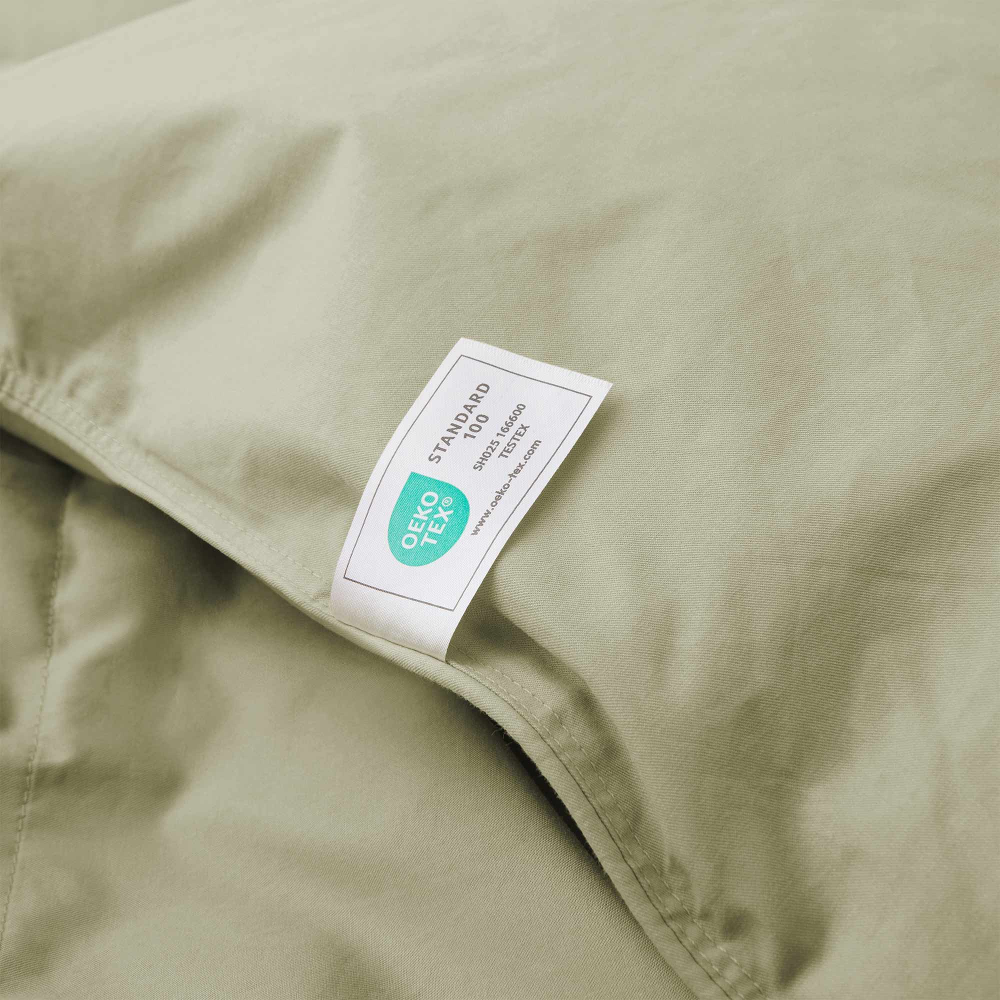 A close-up of the Premium Goose Feather Comforter in light green fabric, featuring an attached OEKO-TEX Standard 100 certification label.