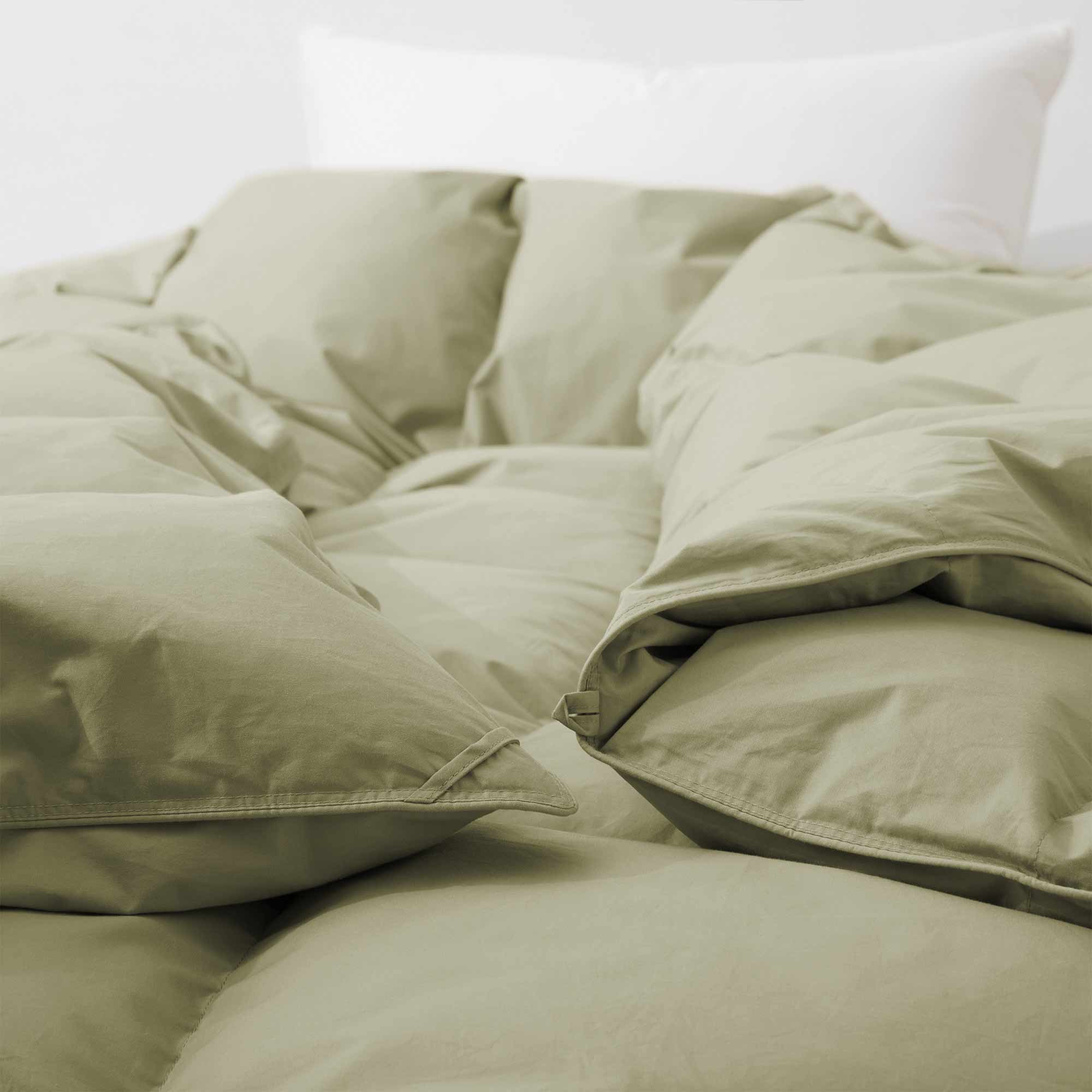 A close-up of the Premium Goose Feather Comforter in light green on a bed, with a white pillow in the background.