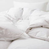 A Premium Goose Feather Comforter and pillow on a bed with soft natural lighting, creating a cozy atmosphere.
