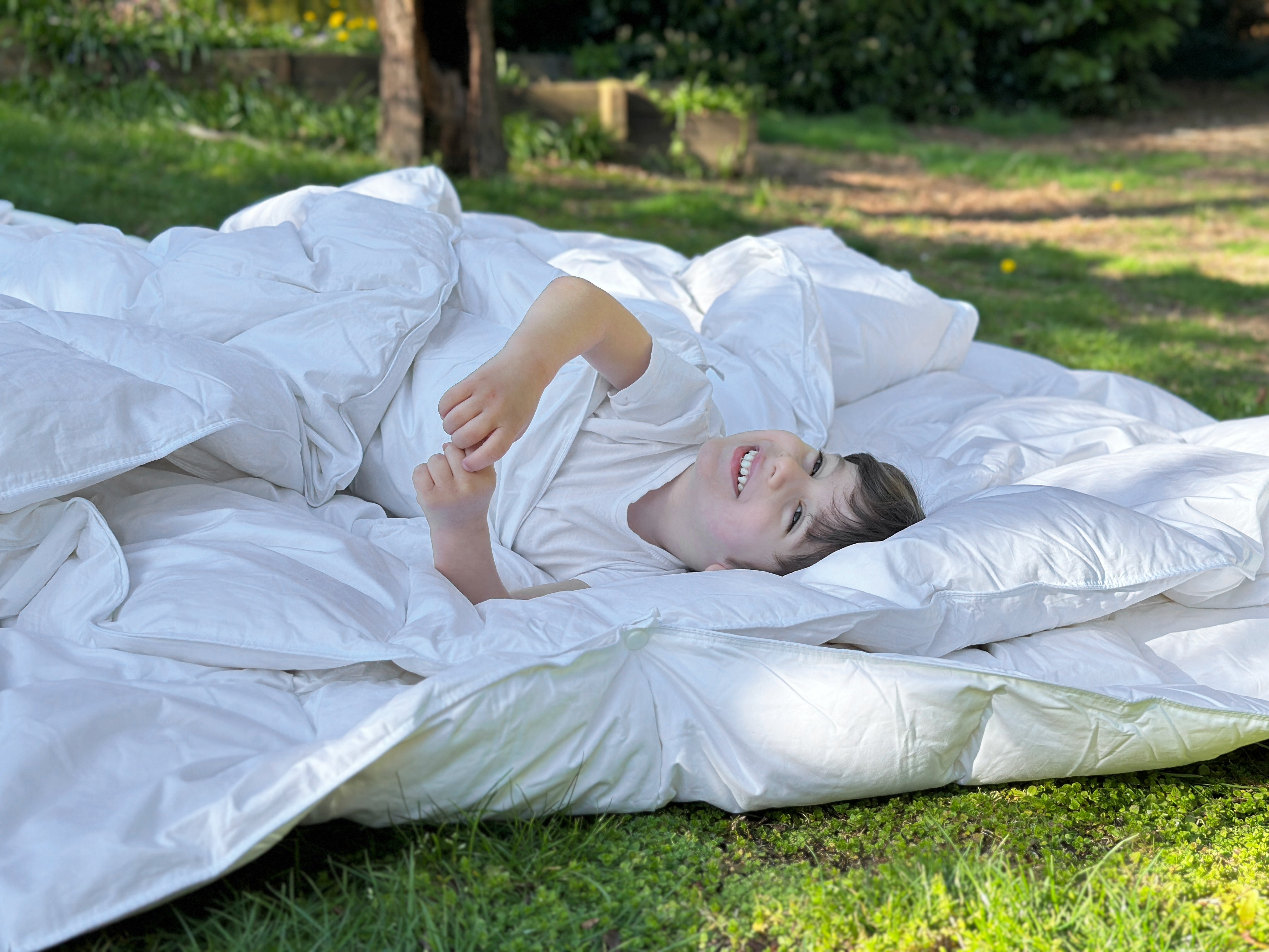 Person lying on a large white comforter in a grassy outdoor setting