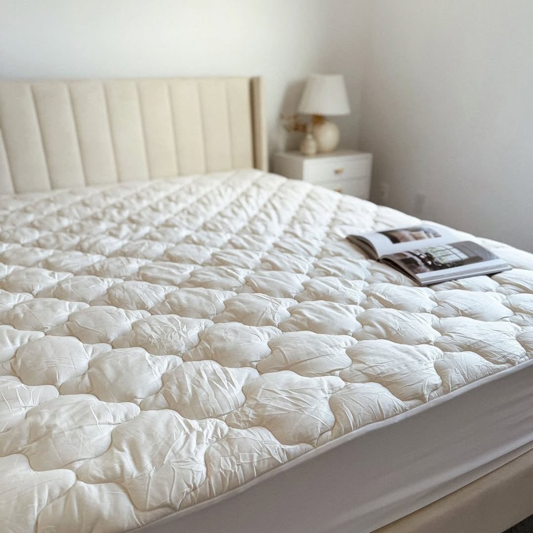 A neatly made bed with a cream headboard, a nightstand, lamp, and an open magazine on the mattress.